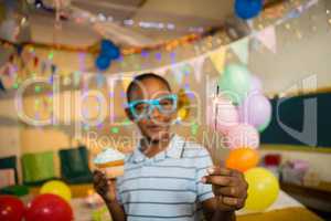 Cute boy holding sparkler and cupcake during birthday party
