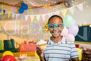 Portrait of cute boy holding cupcake during birthday party