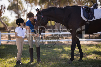 Full length of female jockey with sister feeding horse