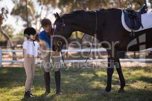 Full length of female jockey with sister feeding horse