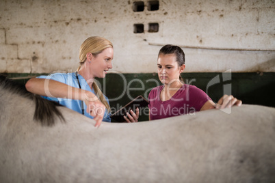Female vet showing tablet computer to woman standing by horse