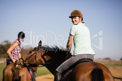 Portrait of female friends looking over shoulder while sitting on horse