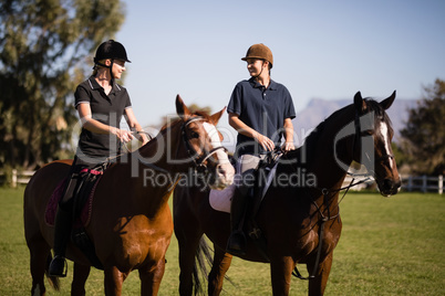 Female friends talking while sitting on horse at barn