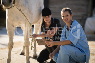 Portrait of vet with jockey crouching by horse