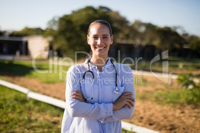 Smiling female vet with arms crossed standing at barn