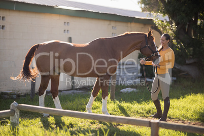 Full length of female jockey with horse standing on field at barn