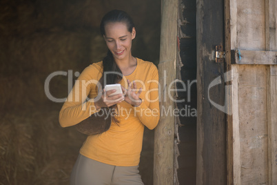 Female jockey using smart phone while standing at stable