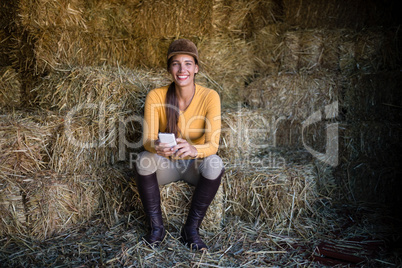 Happy female jockey using phone while sitting on hay in stable