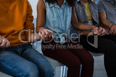 Mid section of friends holding hand while sitting on chair