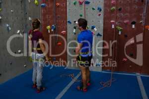 Male trainer guiding woman in climbing wall at gym