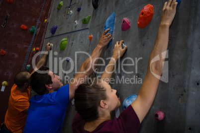Trainer with athletes climbing wall in healthy club