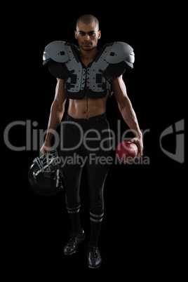 Muscular American football player holding football and head gear in his hand