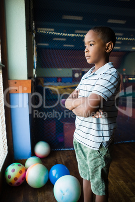 Thoughtful boy standing with arms crossed near window