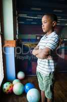 Thoughtful boy standing with arms crossed near window