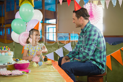 Father and girl playing with toy kitchen set during birthday party