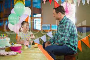 Father and girl playing with toy kitchen set during birthday party
