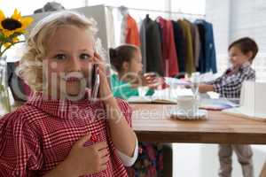 Portrait of businesswoman talking on mobile phone while colleagues working in background