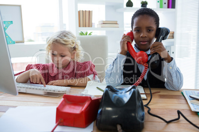 Portrait of businessman talking on phone while colleague using computer