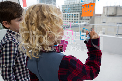 Businesswoman explaining to male colleague while writing on window in office