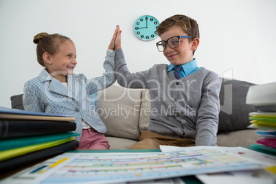 Colleagues giving high five while sitting on sofa in office