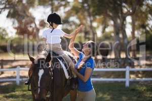 Side view of woman giving high five to girl sitting on horse