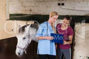 Female vet showing records to woman while standing by horse