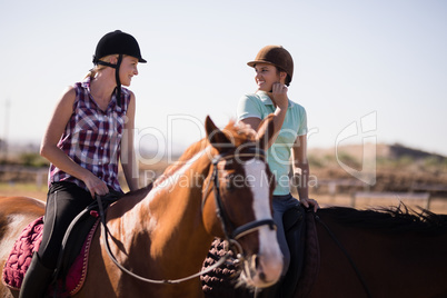 Happy female friends talking while horseback riding