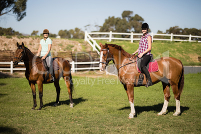 Female friends horseback riding during sunny day