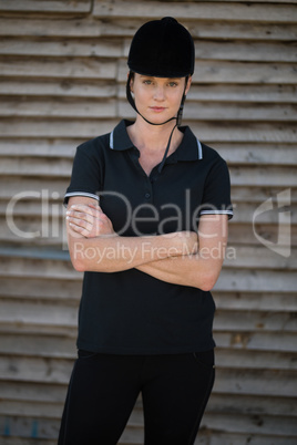 Portrait of female jockey with arms crossed standing by stable