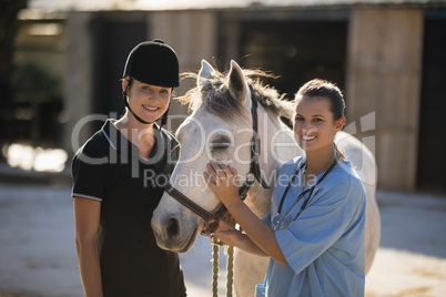 Portrait of smiling female vet with jockey standing by horse