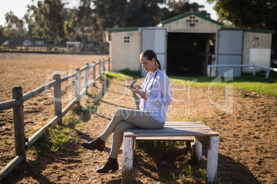 Female vet using digital tablet while sitting at barn