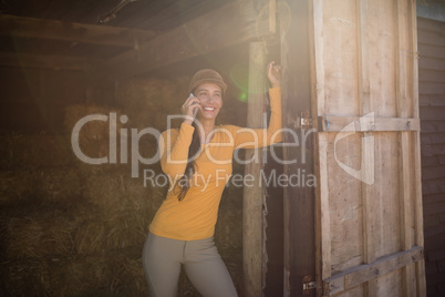 Smiling female jockey talking on mobile phone in stable