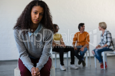 Portrait of serious woman sitting on chair with friends in background