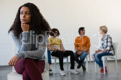 Thoughtful woman sitting on chair with friends in background