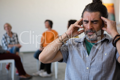 Man with head in hand sitting on chair while friends discussing in background
