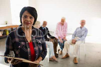 Portrait of senior woman holding clipboard with friends sitting in background