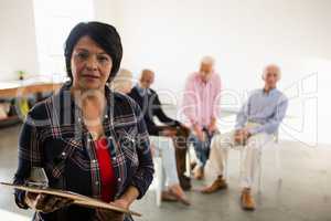 Portrait of senior woman holding clipboard with friends sitting in background