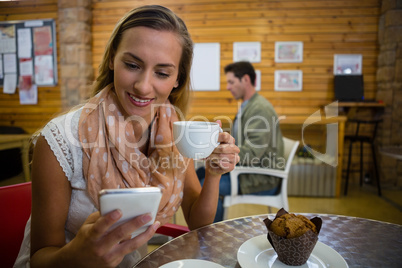 Woman using smart phone while having coffee in cafe