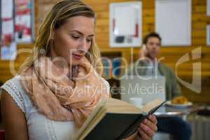 Woman reading book while man talking on phone in background
