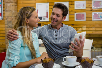 Man showing digital tablet to girlfriend in cafe