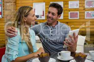 Man showing digital tablet to girlfriend in cafe