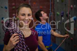 Athlete carrying rope while trainer climbing wall at gym