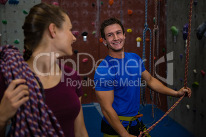Female athlete carrying rope looking at trainer climbing wall