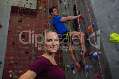 Portrait of female athlete standing against trainer climbing wall