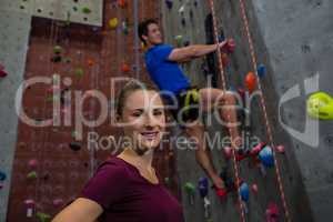 Portrait of female athlete standing against trainer climbing wall
