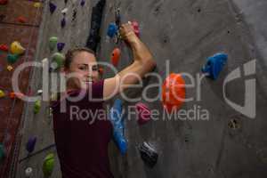 Portrait of confident female athlete climbing wall in gym