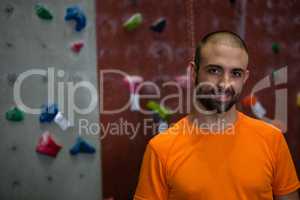 Portrait of confident trainer standing by climbing wall in gym