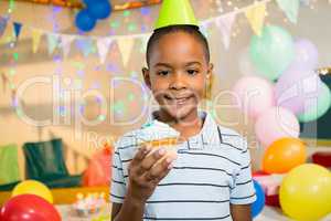 Portrait of cute boy holding cupcake during birthday party