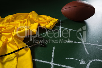 American football jersey, whistle and football lying on green board with strategy drawn on it