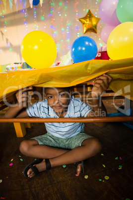 Portrait of cute boy sitting under table